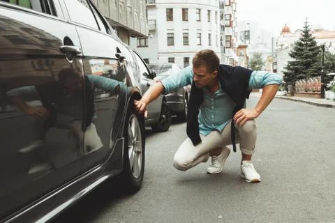 Young handsome man checking wheel of his car having problems on the road Stock Photos