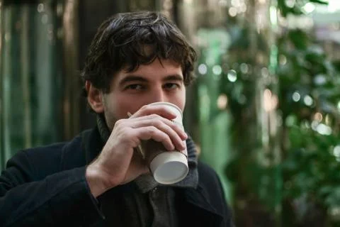 Young handsome man in coat drinking coffee looking at camera Stock Photos
