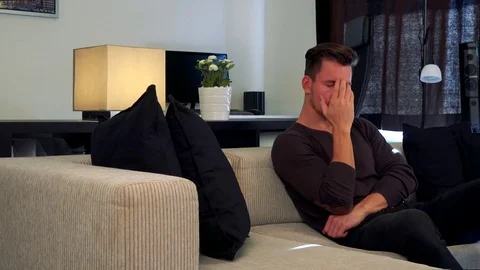 A young, handsome man on a couch covers his face with a palm, disappointed Stock Footage