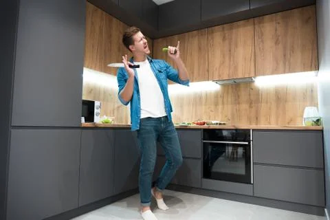 Young handsome man dancing while cooking in the kitchen Stock Photos