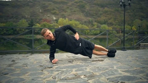 A young handsome man doing side plank touching ground on a terrace near the pond Stock Footage 70345162