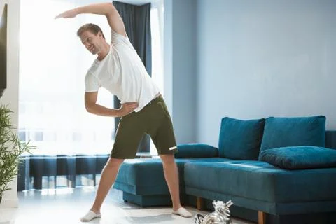 Young handsome man doing sideways during warm up before workout at home looking Stock Photos