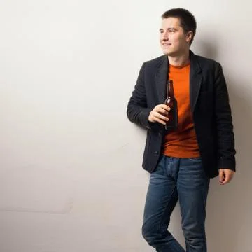 Young handsome man drinking bear from glass bottle standing near wall at the  Stock Photos