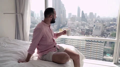 Young, handsome man drinking coffee close to the window with splendid city view, Stock Footage 92612048