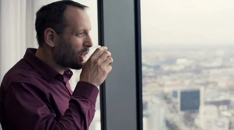 Young, handsome man drinking juice and enjoy city view from the window Stock Footage 63982178