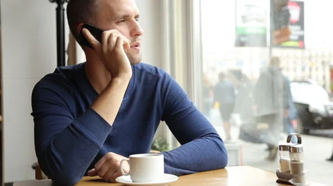 Young handsome man drinking tea and talking on the cellphone in the cafe Stock Footage 67863401