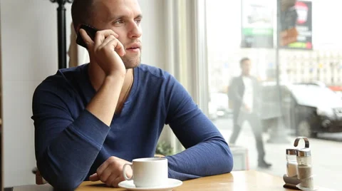 Young handsome man drinking tea and talking on the cellphone in the cafe Stock Footage 67863446