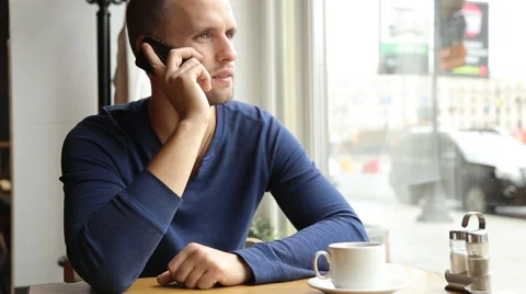 Young handsome man drinking tea and talking on the cellphone in the cafe Stock Footage 67863500