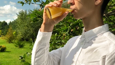 Young handsome man drinks orange juice and smile in the garden enjoying life. 스톡 동영상 115374912