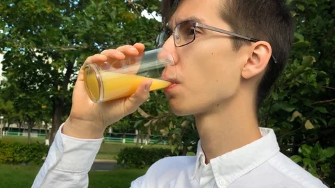 Young handsome man drinks orange juice and smile in the garden enjoying life. 스톡 동영상 115374919