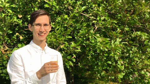 Young handsome man drinks orange juice and smile in the garden enjoying life. 스톡 동영상 115374925