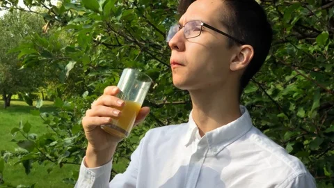 Young handsome man drinks orange juice and smile in the garden enjoying life. 스톡 동영상 115374945