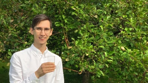 Young handsome man drinks orange juice and smile in the garden enjoying life. Stock Footage 115374956