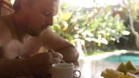 Young handsome man eating oat porridge has breakfast sitting on his villa on Stock Footage 92740904
