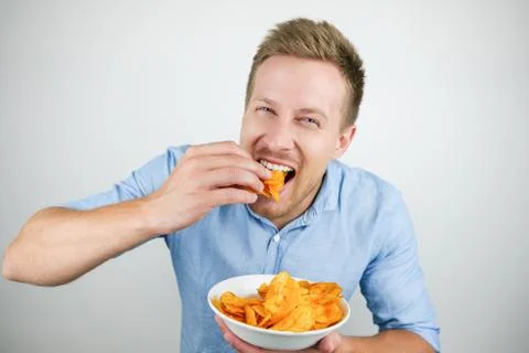 Young handsome man eats chips on isolated white background Stock Photos