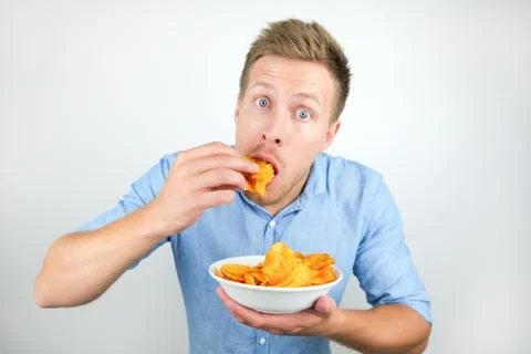 Young handsome man eats chips with paprika from plate on isolated white Stock Photos