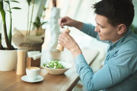 Young handsome man eats salad and drinks coffee for lunch during break at cafe Stock Photos