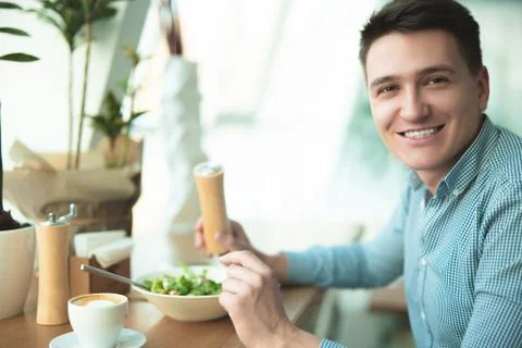 Young handsome man eats salad and drinks coffee for lunch during break at cafe Stock Photos