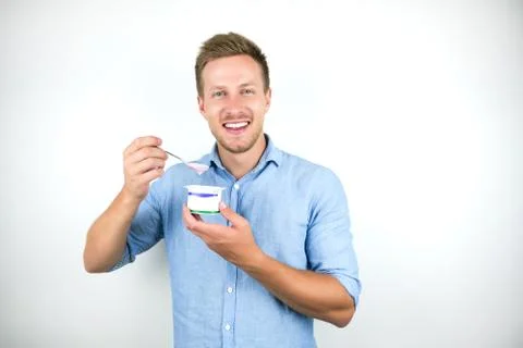 Young handsome man eats yogurt with spoon smiling on isolated white background Stock Photos