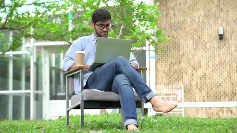 Young handsome man freelancer sitting on chair in front yard  using laptop co Stock Footage 134399628