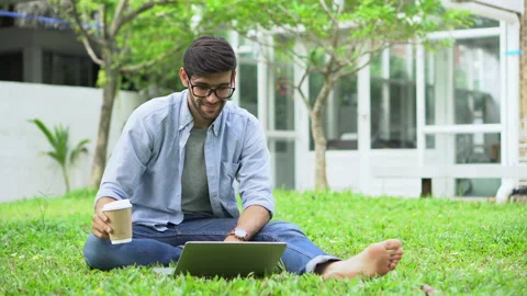 Young handsome man freelancer sitting on grass using laptop computer with cof Stock Footage 134400087