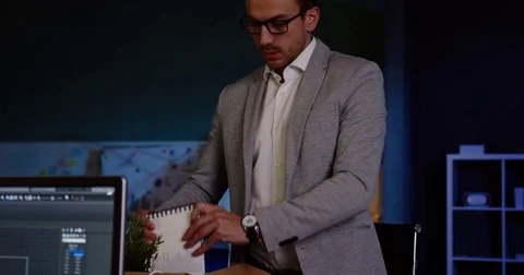 Young handsome man in glasses packing his stuff in the office late at night Stock Footage 82446995