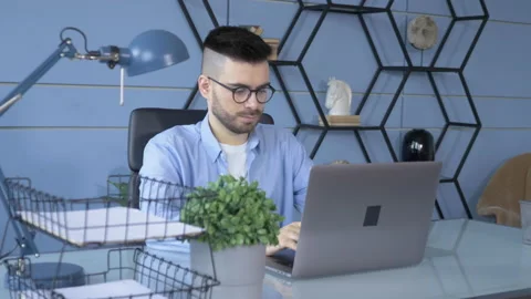 Young handsome man in glasses working on his laptop and sitting in the office Stock Footage 146319949