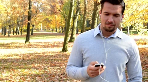 A young handsome man goes through the woods and listens to music from headphones Stock Footage 59725940