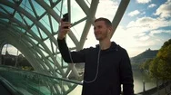 Young Handsome Man With Headphones Making A Video Call On The Bridge Slow Motion Stock Footage
