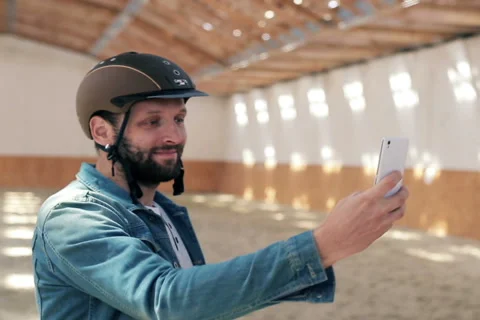 Young, handsome man with helmet taking selfie photo on the stable NTSC Stock-Footage 49976360