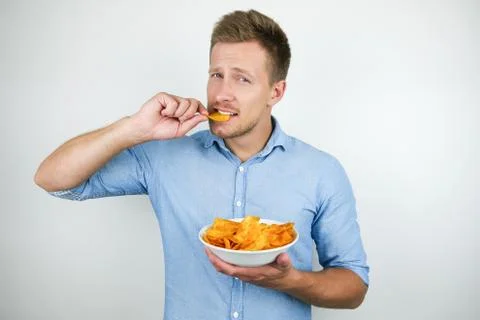 Young handsome man holding plate with chips putting chips with paprika in his Stock Photos