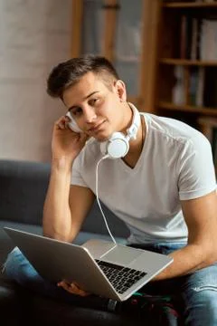 Young handsome man with laptop on gray sofa at home Stock Photos