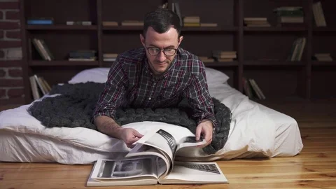 Young handsome man lies on a bed and reads a book Stock Footage 84846313