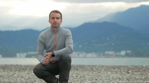 Young handsome man looking into the camera and smiles on the rocky beach. Behind Video stock 67610447