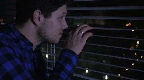 Young handsome man looking out of the window through the blinds. 動画素材 57633332