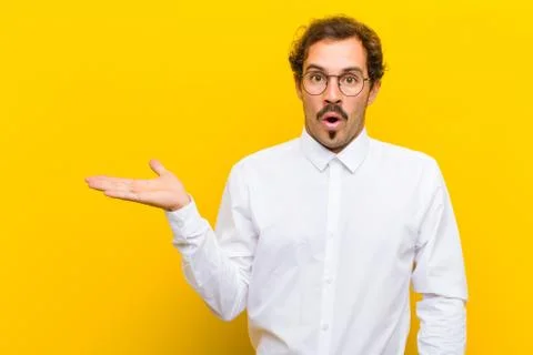 Young handsome man looking surprised and shocked, with jaw dropped holding an Stock Photos