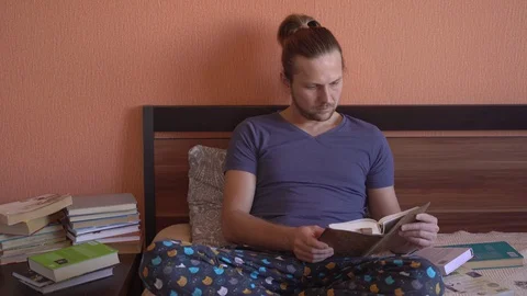 Young handsome man is lying on bed and reading . A lot of free time, many books Stock Footage 128005170