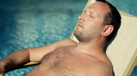 Young handsome man lying on sunbed and taking sunbath by the pool Stock Footage 1097021