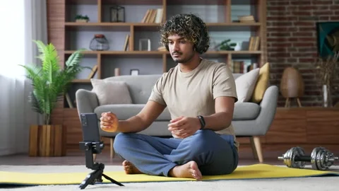 Young handsome man meditates during an online course on phone while sitting 스톡 동영상 334231004