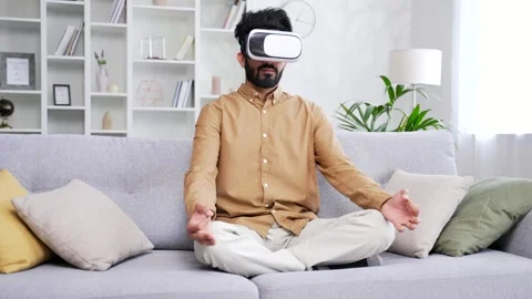 Young handsome man meditating using VR glasses while sitting on sofa in living  Stock Footage 252215063