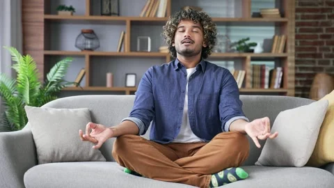 Young handsome man meditating while sitting on sofa in living room at home.  Stock Footage 296763958