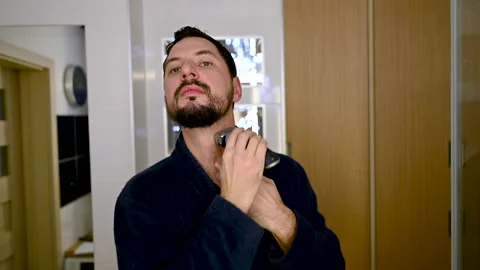 Young handsome man in men's bathrobe is shaving in front of the bathroom mirror Stock Footage 169249728