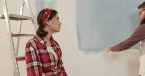 Young handsome man paints wall in room to blue while the girl sits on the ladder Stock Footage 147060090