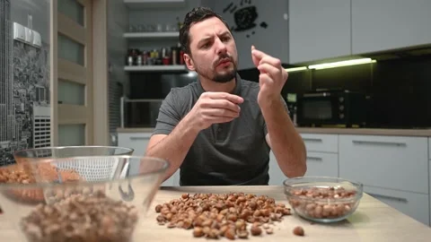 Young handsome man peels hazelnuts in his kitchen. Smiling Stock Footage 169191836