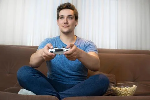 Young handsome man playing video game sitting on comfy sofa holding joystick Stock Photos