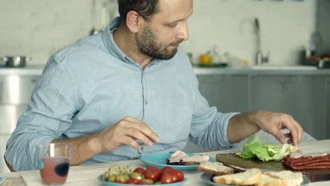 Young, handsome man preparing sandwich for breakfast on wooden table Vídeo Stock 74153446