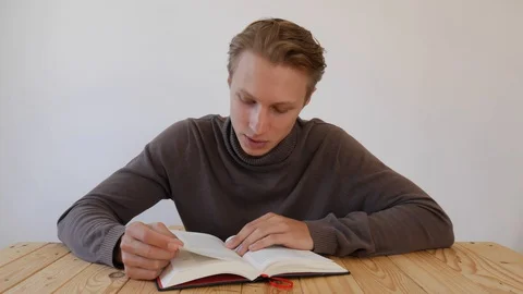 Young handsome man reading a book out loud and looking at camera. Student Video stock 129010515