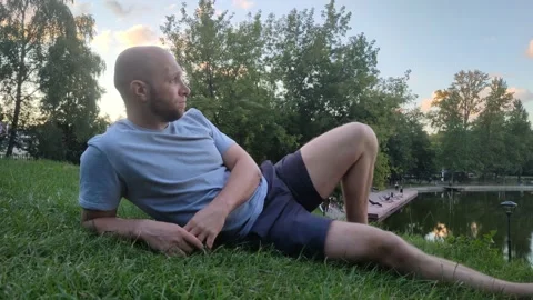 Young handsome man is resting in a clearing near lake or river Vidéo 215072816