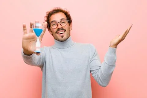 Young handsome man with a sand clock timer against pink flat wall Stock Photos