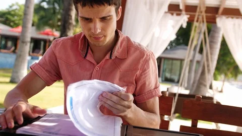 Young handsome man sits in a cafe on the beach scrolls through the menu, wants Stock Footage 90980174